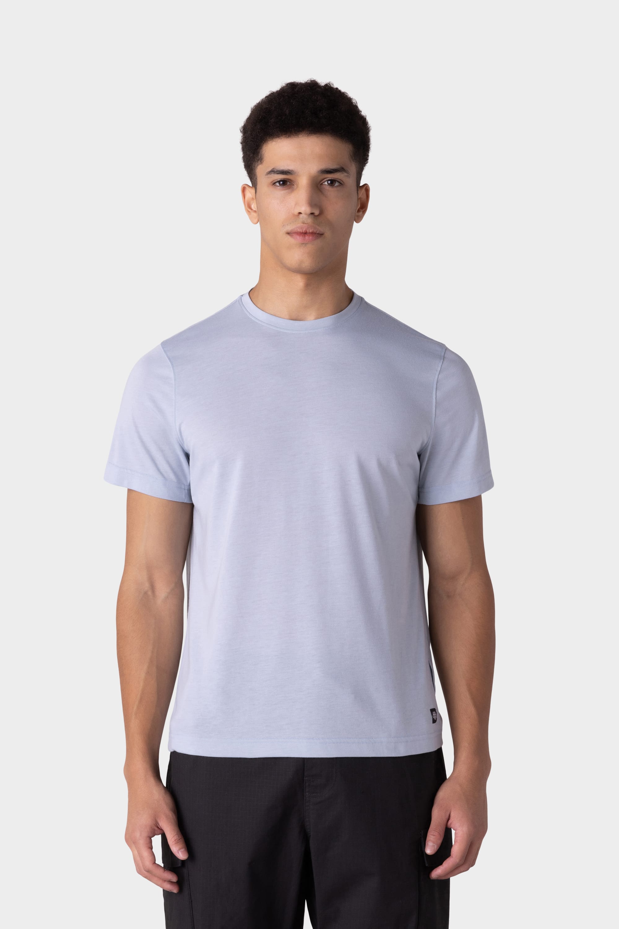 A young man with short dark hair wears the 686 Mens Everywhere drirelease® Tech Tee in light gray and black pants, standing against a plain white background, facing forward with a neutral expression.