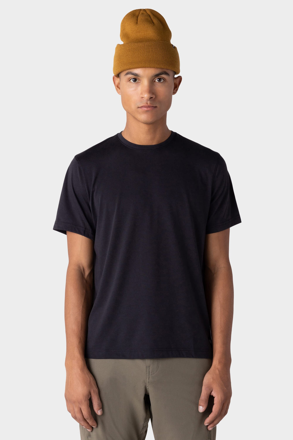 A person stands facing forward, wearing a mustard yellow beanie, light brown pants, and the 686 Mens Everywhere drirelease® Tech Tee by 686, against a plain light gray background.