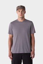 A man wearing the 686 Mens Everywhere drirelease® Tech Tee, black pants, and a taupe cap stands facing forward against a light gray background.