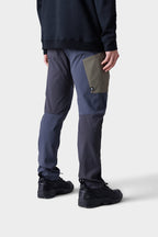 A person faces away from the camera in 686 Men's Anything Cargo Pant - Slim Fit by 686, featuring 13 pockets in blue, gray, and olive, paired with black sneakers and a black long-sleeve top against a light background—adventure-ready style.