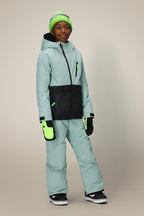 A child in the 686 Boys' Hydra™ Insulated Jacket, coordinated blue and black pants, neon green beanie, and mittens stands against a plain beige background.