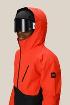 A boy wears the 686 Boys' Hydra™ Insulated Jacket in bright red and black by 686, paired with black ski goggles and a helmet, facing slightly to the side against a plain beige background.