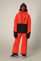 A young boy poses confidently against a plain, light background wearing the 686 Boys' Hydra™ Insulated Jacket in bright orange and black, with matching pants, black gloves, a black beanie with a red stripe, and black-and-white sneakers.