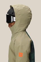 A boy in the 686 Boys' Hydra™ Insulated Jacket, tan with an orange patch and body-mapped lining, wears a black ski helmet and large black goggles, shown in profile against a plain light background. Brand: 686.