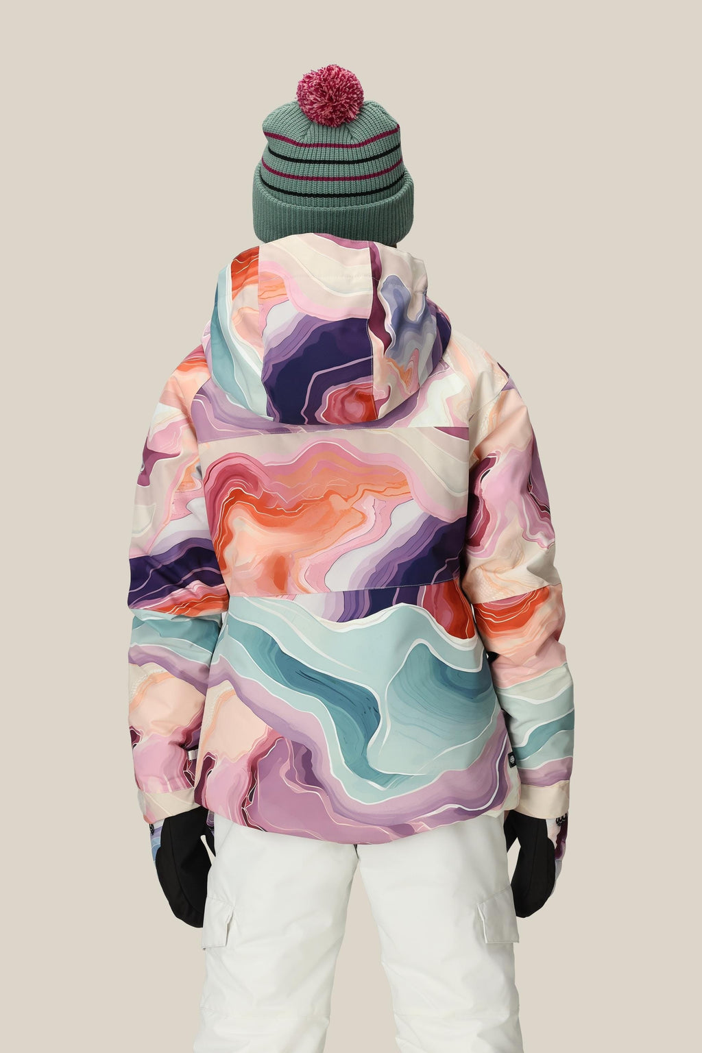 Someone wearing the 686 Girls' Athena™ Insulated Jacket stands with their back to the camera, paired with white snow pants, black gloves, and a green beanie featuring a red pom-pom against a plain background.