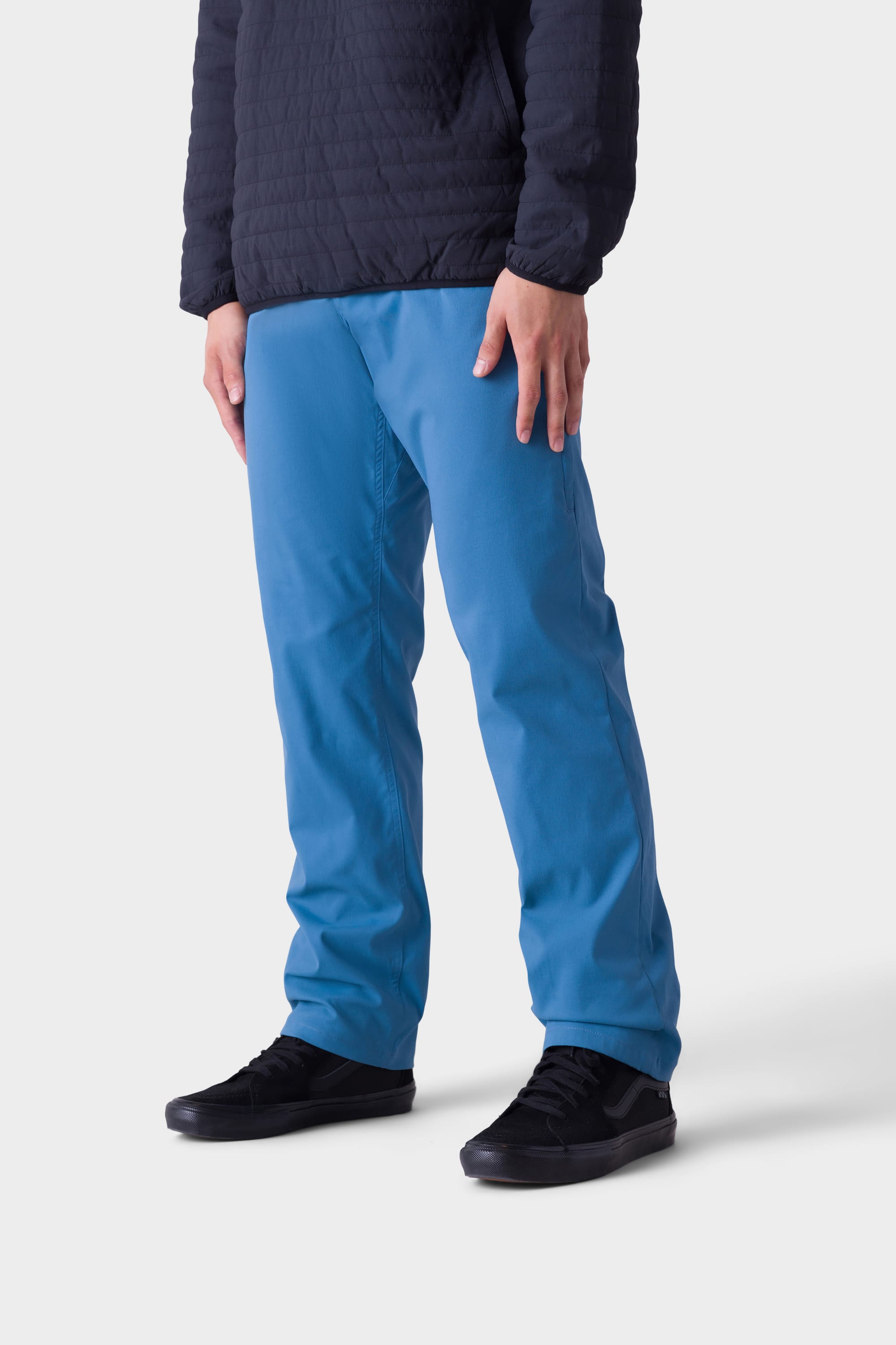 A person showcases the 686 Men's Everywhere® Merino-Lined Pant - Relaxed Fit, paired with a stylish insulated jacket and black sneakers, against a plain light background. The image is cropped below the shoulders to emphasize the pants and shoes.