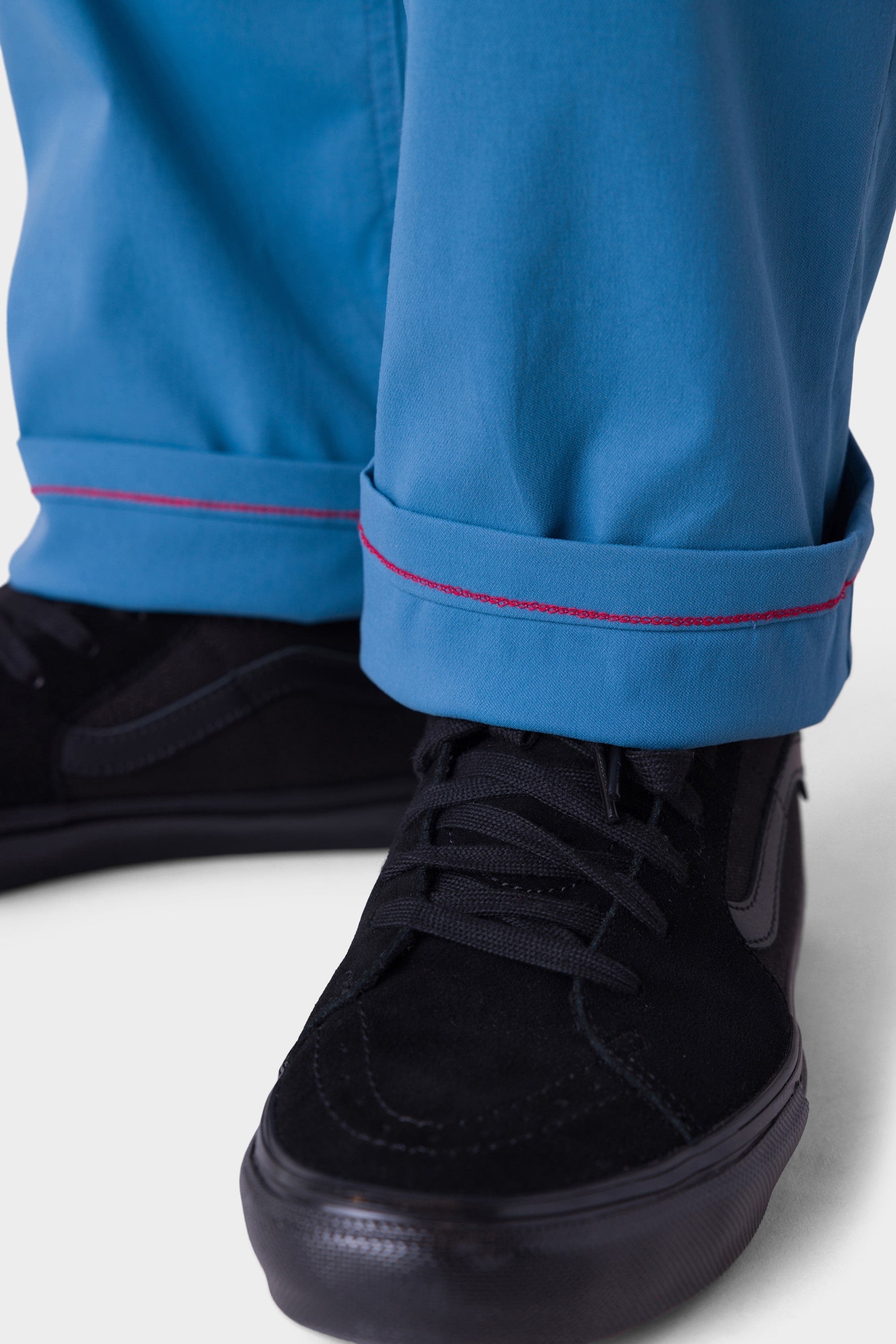 Close-up of a person wearing 686 Men's Everywhere® Merino-Lined Pant - Relaxed Fit, featuring red cuff stitching, paired with black suede sneakers and a stylish insulated jacket—ideal for showcasing the detail and staying warm.