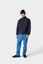 A person wearing a black beanie, stylish insulated outerwear, 686 Men's Everywhere® Merino-Lined Pant - Relaxed Fit in blue, and black shoes stands against a plain white background, looking at the camera with a neutral expression.