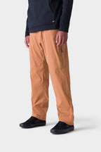 A person stands against a plain white background wearing 686 Men's Everywhere® Merino-Lined Pant - Relaxed Fit in light brown, a black hoodie under an insulated outerwear, and black sneakers. The image is cropped at the shoulders.
