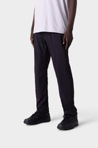 Only the lower half of the person is visible as they stand against a light gray background, wearing 686 Men's Everywhere® Merino-Lined Pant - Slim Fit by 686, paired with black sneakers for warmth in colder conditions.