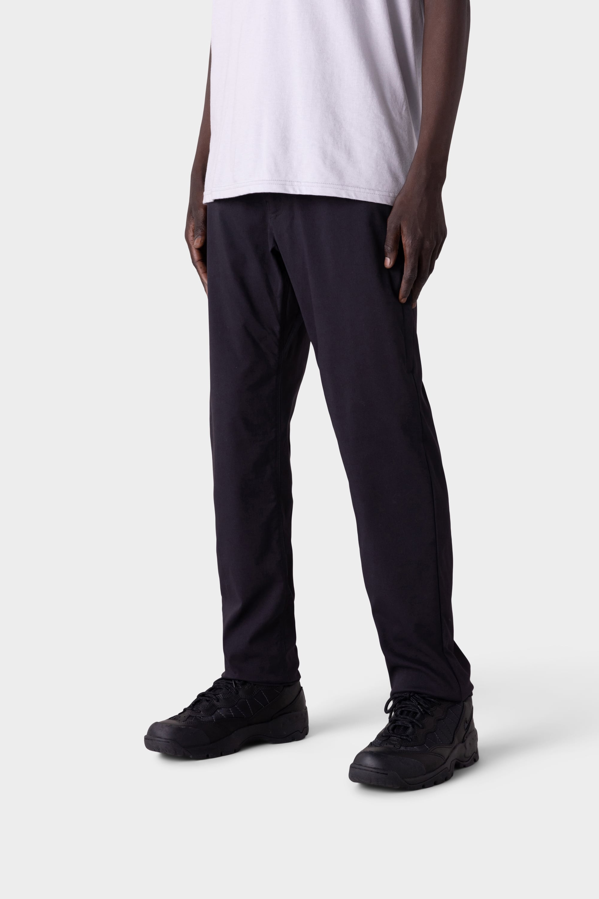 Only the lower half of the person is visible as they stand against a light gray background, wearing 686 Men's Everywhere® Merino-Lined Pant - Slim Fit by 686, paired with black sneakers for warmth in colder conditions.