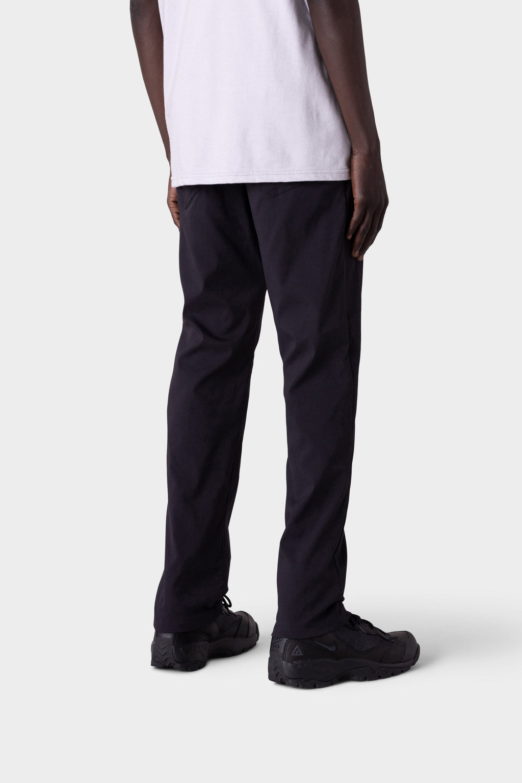 A person shown from the back wears the 686 Men's Everywhere® Merino-Lined Pant - Slim Fit in black with a white T-shirt and black sneakers, standing against a plain light gray background—perfect for layering to stay warm and dry.