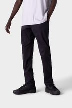 A person stands at an angle against a light gray background, wearing the 686 Men's Everywhere® Merino-Lined Pant - Slim Fit with one hand in a pocket—ideal for warmer or dry conditions.