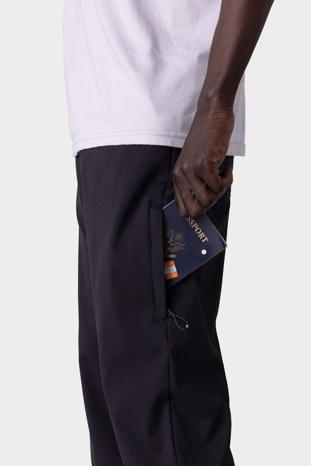 A person wearing a white shirt and 686 Men's Everywhere® Merino-Lined Pant - Slim Fit holds a blue passport partially out of their pocket, ready for travel to colder climates, against a plain light background.