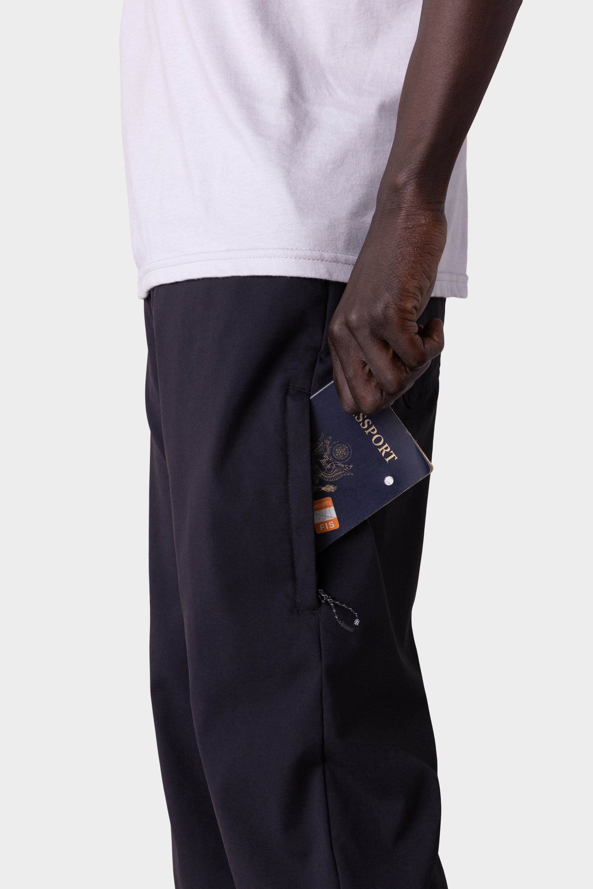 A person wearing a white shirt and 686 Men's Everywhere® Merino-Lined Pant - Slim Fit holds a blue passport partially out of their pocket, ready for travel to colder climates, against a plain light background.