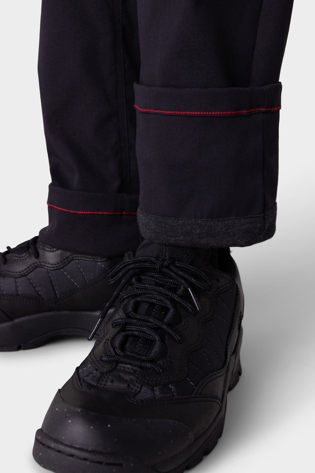 Close-up of a person wearing 686 Men's Everywhere® Merino-Lined Pant - Slim Fit with red-stitched, rolled cuffs, dark socks, and black lace-up sneakers—ideal from 686 for warmth and dryness in colder conditions.