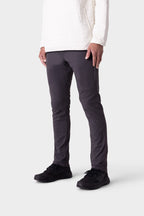 Wearing 686 Men's Everywhere® Merino-Lined Pant - Slim Fit in dark gray, paired with a white long-sleeve and black sneakers, a person stands against a plain light gray background. The image is cropped above the shoulders.