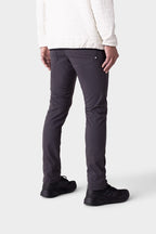 A person stands facing away in 686 Men's Everywhere® Merino-Lined Pant - Slim Fit (dark gray), pairing warmth and style, with a white quilted jacket and black sneakers, shown from the back and side against a plain light background.