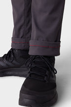 Close-up of a person wearing 686 Men's Everywhere® Merino-Lined Pant - Slim Fit in dark gray with red-stitched cuffs, rolled above black athletic shoes; these pants keep you warm and dry in cold weather.
