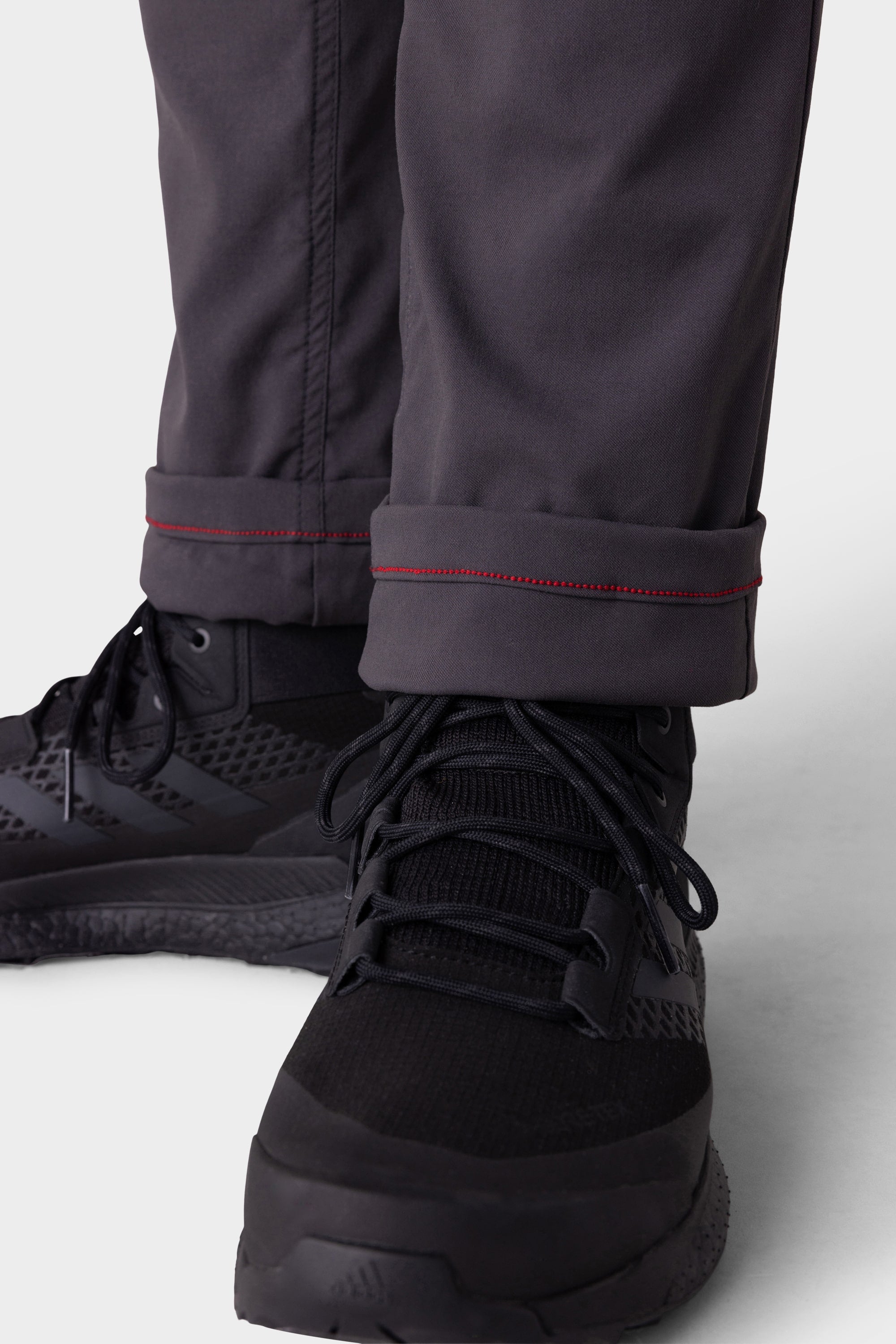 Close-up of a person wearing 686 Men's Everywhere® Merino-Lined Pant - Slim Fit in dark gray with red-stitched cuffs, rolled above black athletic shoes; these pants keep you warm and dry in cold weather.