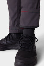 Close-up of a person wearing 686 Men's Everywhere® Merino-Lined Pant - Slim Fit, featuring dark gray fabric, red stitching, and soft merino lining at the cuff—ideal for warmth in cold weather—paired with black athletic shoes.