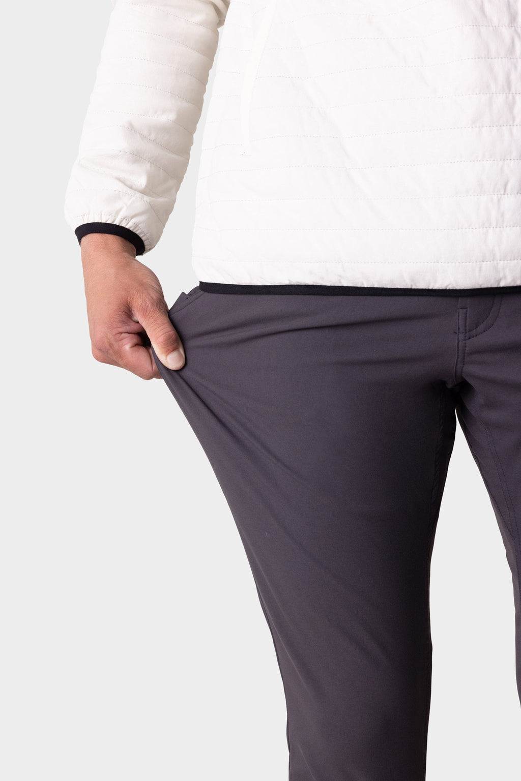 A person wearing a white jacket and dark pants pulls at their 686 Men's Everywhere® Merino-Lined Pant - Slim Fit, showing the stretchy fabric designed to keep you warm and dry in cold conditions.