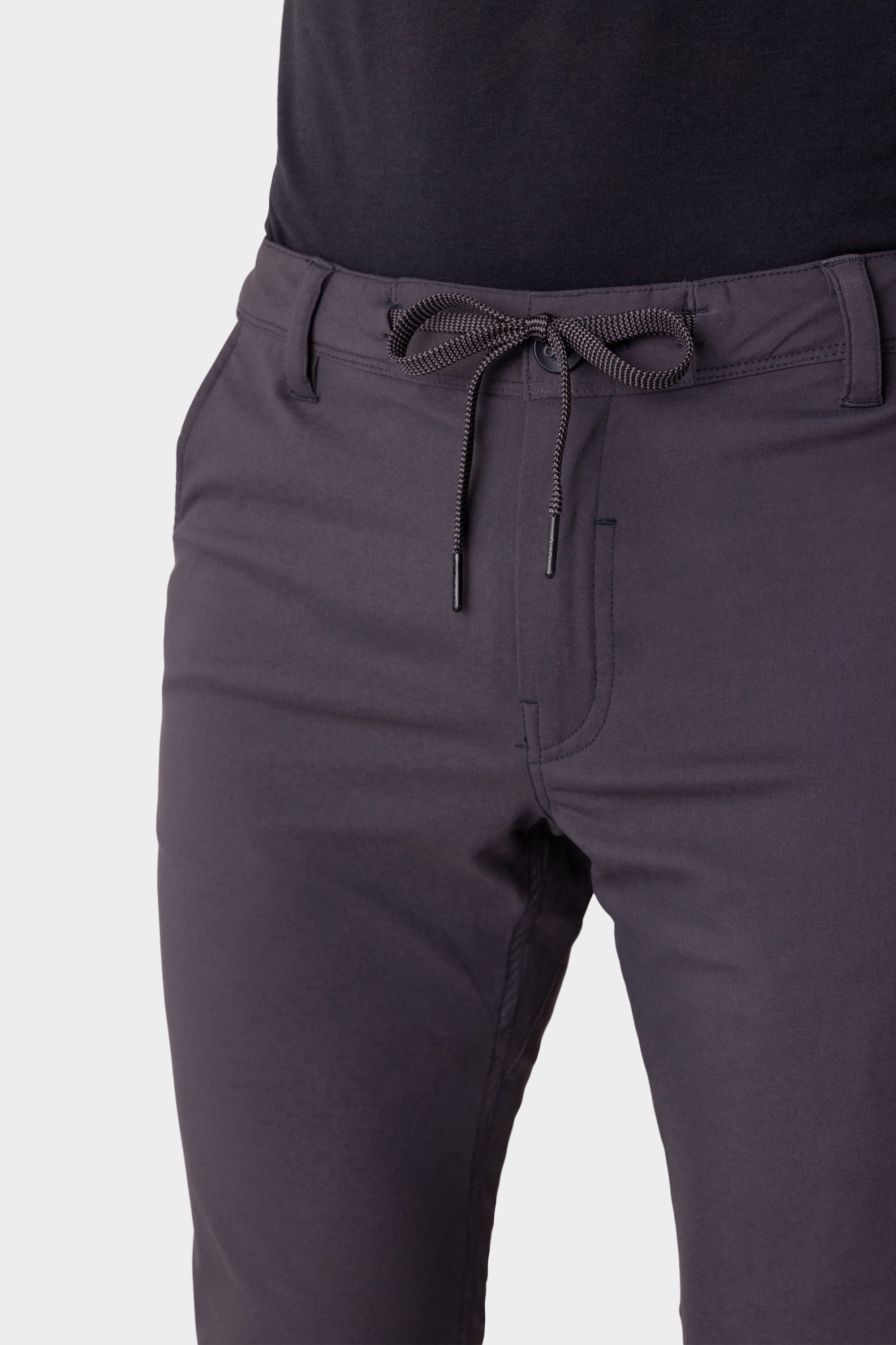 Shown from waist to mid-thigh, a person wears 686 Men's Everywhere® Merino-Lined Pant - Slim Fit in dark gray with hands in pockets and a black top—ideal for warmth and comfort in cold weather.