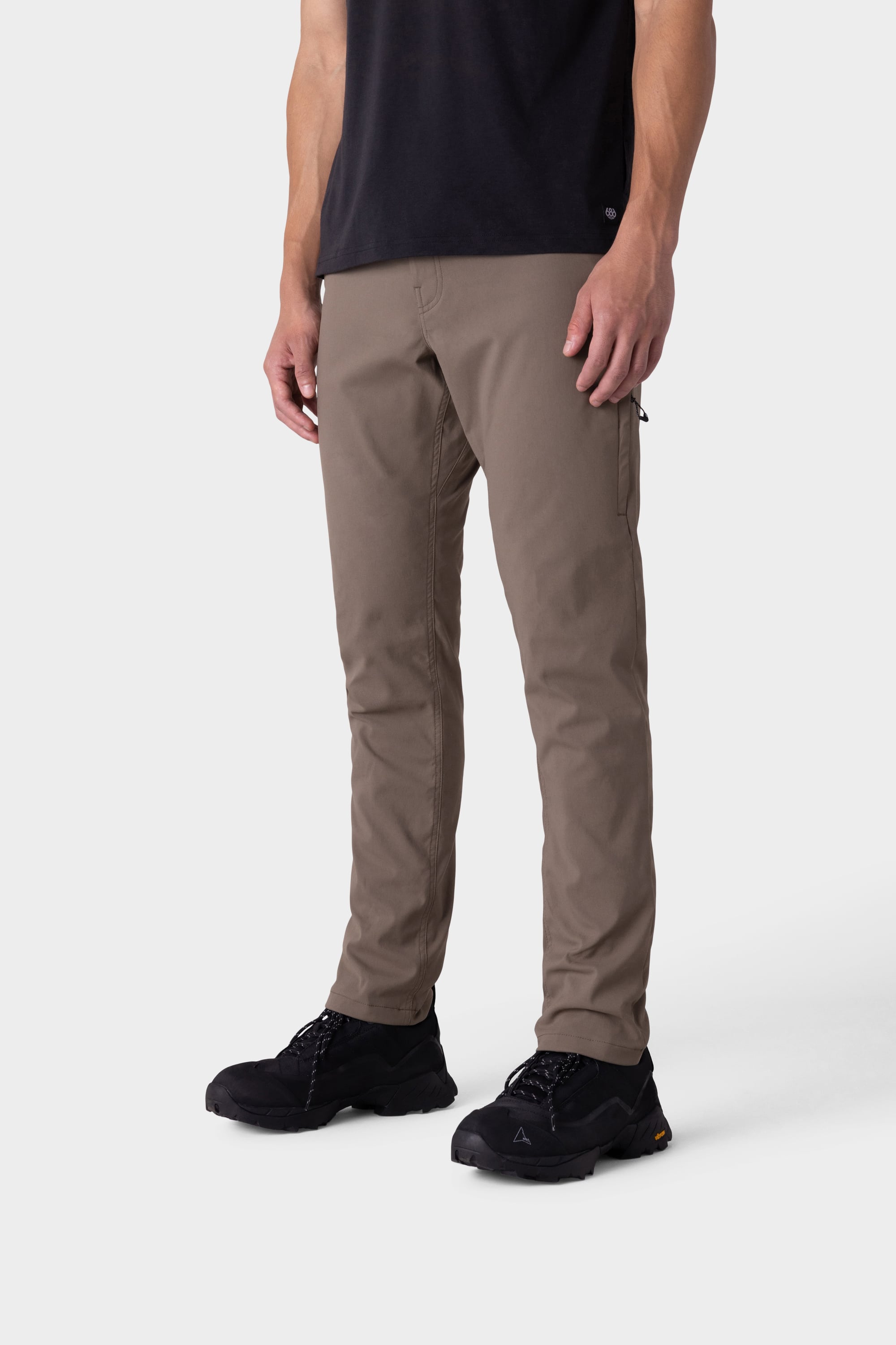 A person wearing a black t-shirt, black sneakers, and 686 Men's Everywhere® Merino-Lined Pant - Slim Fit in khaki stands against a plain white background. The photo is cropped from shoulders down, showing an outfit suited for warm, dry weather.