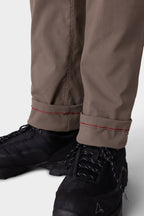 Close-up of a person in 686 Men's Everywhere® Merino-Lined Pant - Slim Fit in light brown with red-stitched cuffs, paired with black athletic shoes—designed by 686 to keep you warm and dry in colder conditions.