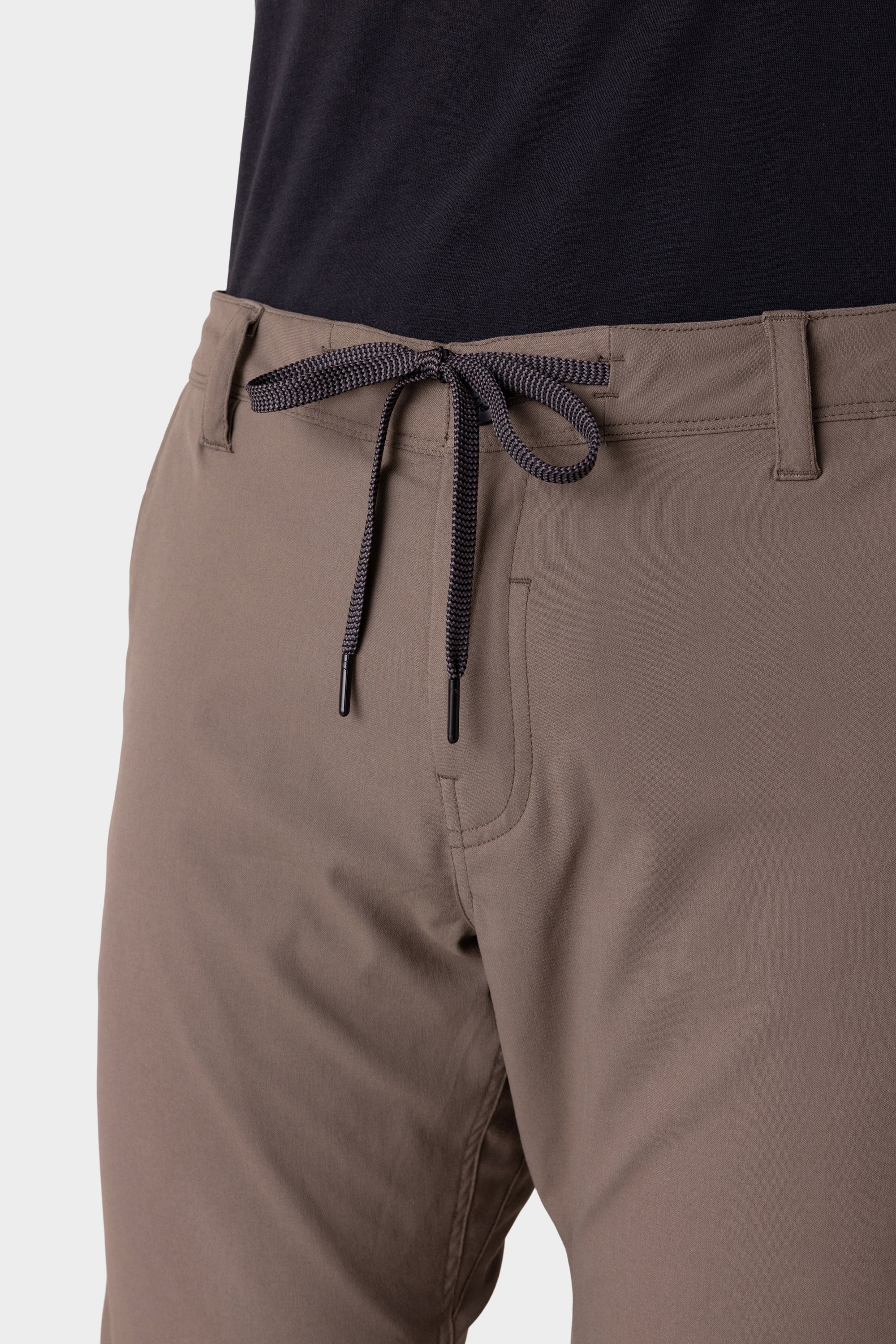 Close-up of a person wearing the 686 Men's Everywhere® Merino-Lined Pant - Slim Fit in taupe, featuring a black and white drawstring, front pockets, and belt loops. These pants keep you warm and dry—ideal for colder conditions.