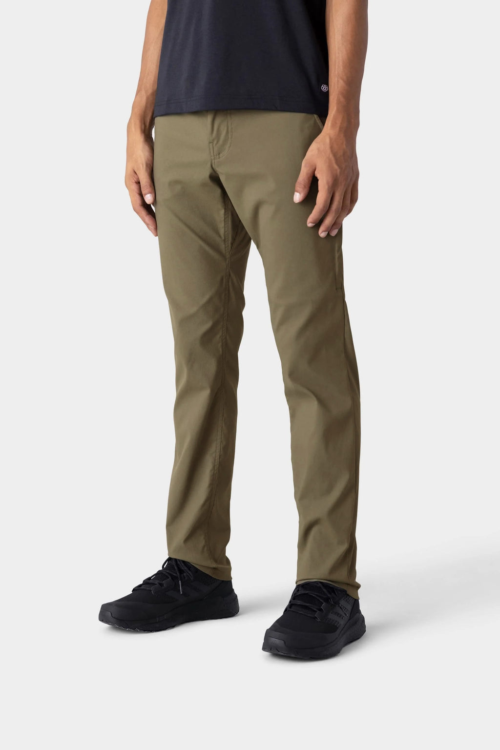 A person wearing 686 Men's Everywhere® Merino-Lined Pant - Slim Fit in olive stands against a plain, light gray background. Cropped below the shoulders, they're also dressed in a black shirt and black shoes—an outfit ideal for colder weather.