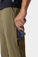 Wearing the 686 Men's Everywhere® Merino-Lined Pant - Slim Fit, a person in olive green places a blue passport into their front pocket, ready to stay warm and dry in colder conditions. The shot highlights their hand, the pocket, and the passport.