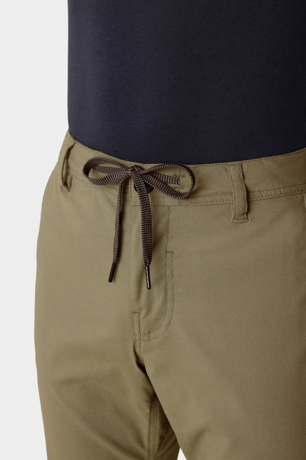 Close-up of a person wearing 686 Men's Everywhere® Merino-Lined Pant - Slim Fit in light brown, featuring a black drawstring belt. Paired with a tucked-in dark shirt, these pants from 686 are perfect for warmth in colder conditions.