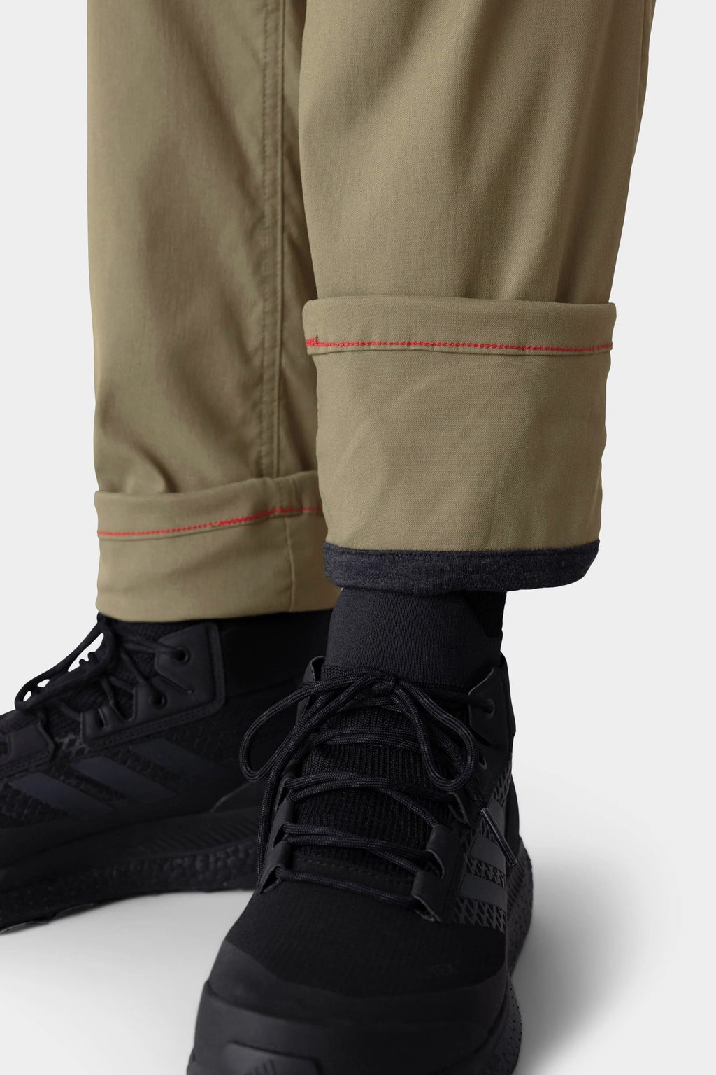 Close-up of a person's lower legs wearing 686 Men's Everywhere® Merino-Lined Pant - Slim Fit with visible red stitching, paired with black socks and athletic shoes—ideal for warmth and dryness in cold conditions.