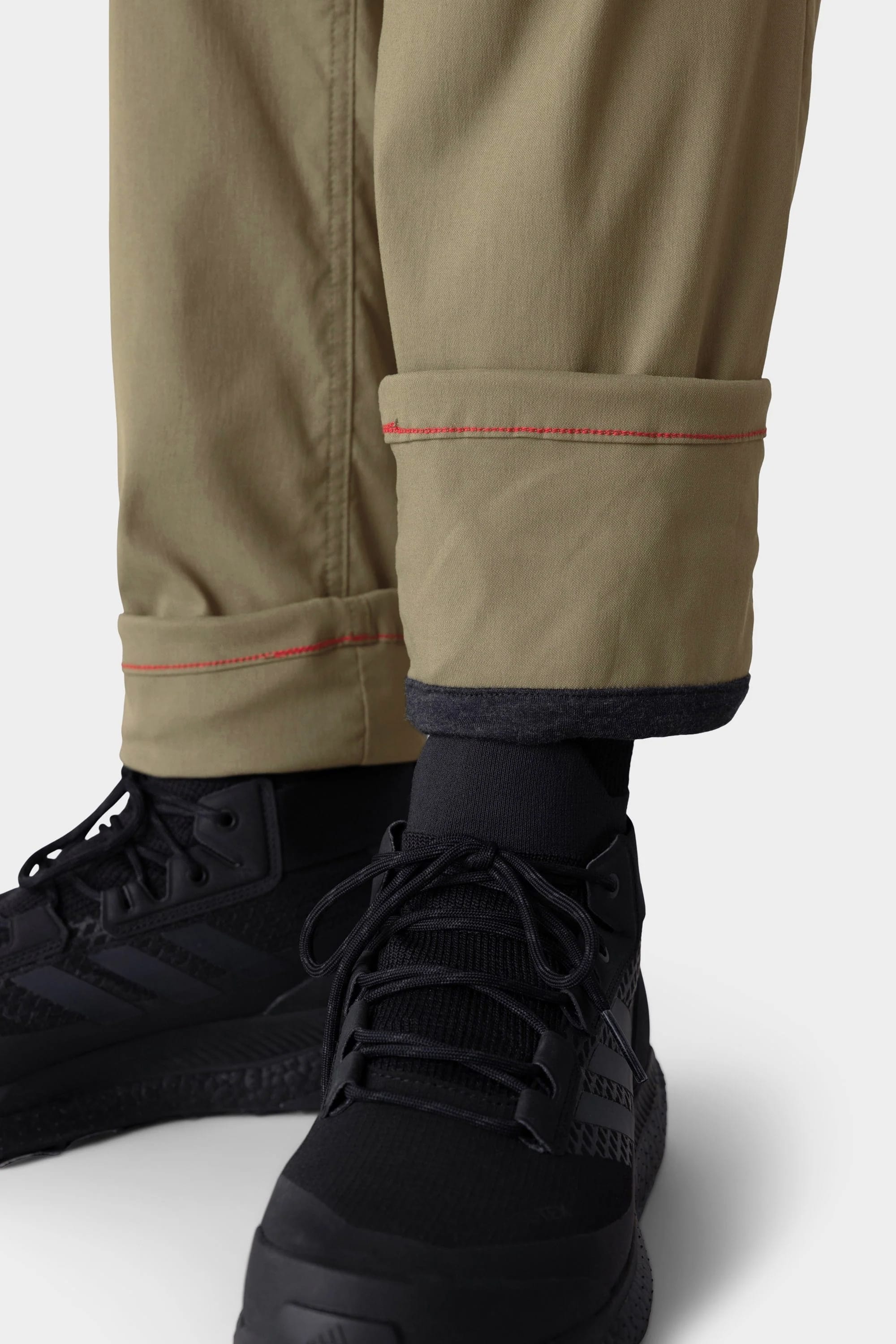 Close-up of a person's lower legs wearing 686 Men's Everywhere® Merino-Lined Pant - Slim Fit with visible red stitching, paired with black socks and athletic shoes—ideal for warmth and dryness in cold conditions.