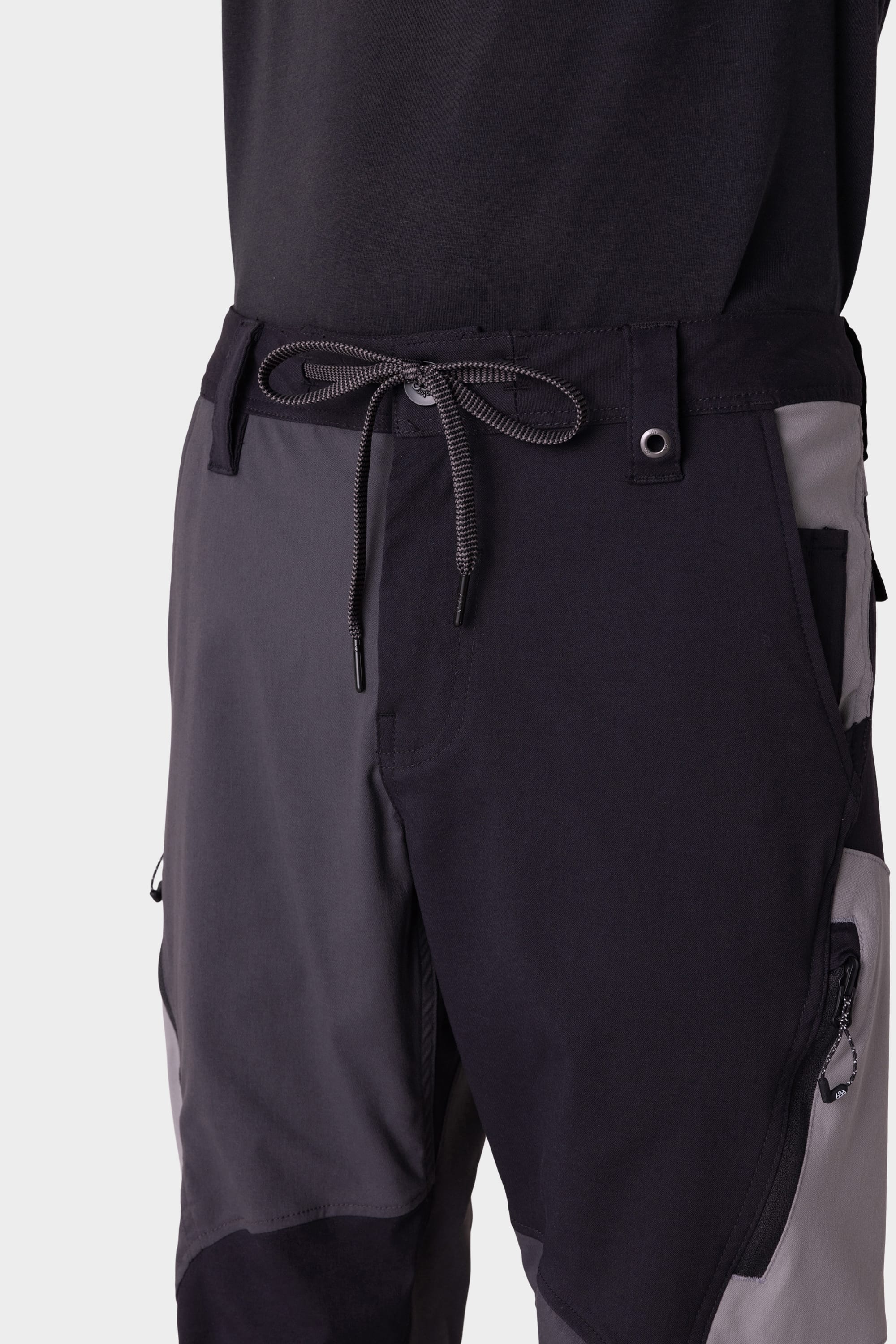 A close-up of a person in the 686 Men's Anything Cargo Pant - Slim Fit by 686, featuring color-blocked black and gray design, drawstring waist, and multiple pockets, paired with a black top, ready for adventure.