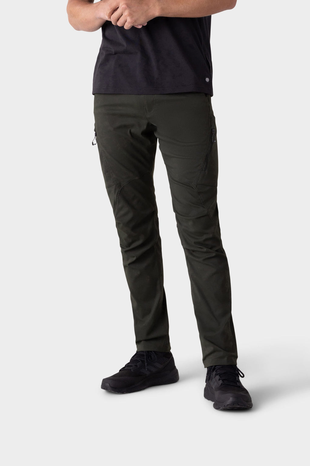 A person stands with arms crossed, wearing a black t-shirt, 686 Men's Anything Cargo Pant - Slim Fit by 686, and black sneakers against a plain white background. The face and upper part of the head are not visible—ready for any adventure.