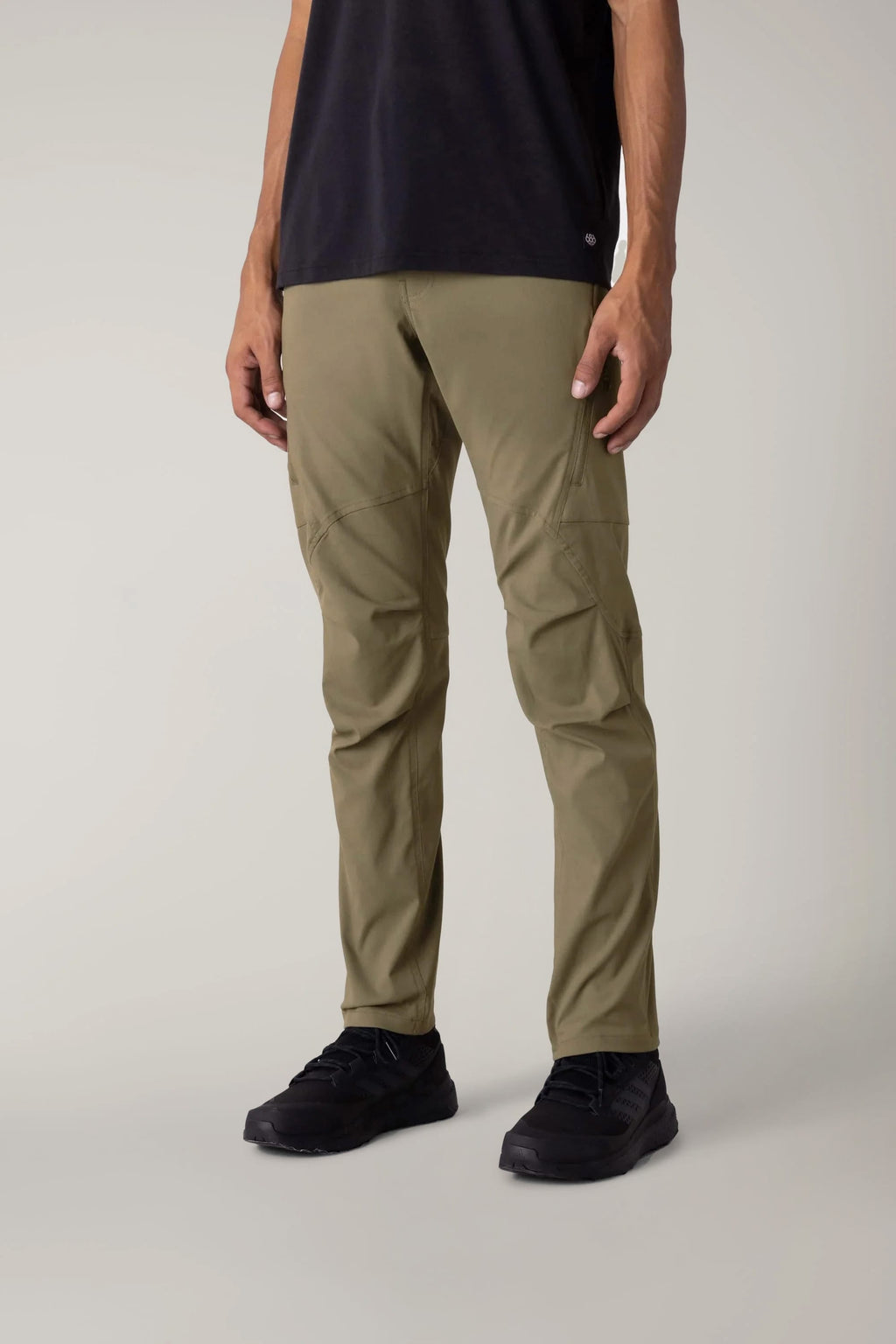 A person in 686 Men's Anything Cargo Pant - Slim Fit (olive green), a black tee, and black sneakers stands against a plain light background. The cropped image highlights the adventure-ready 13-pocket design by 686.