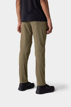 A person stands with their back to the camera against a light gray background, wearing 686 Men's Anything Cargo Pant - Slim Fit in olive green, paired with a black shirt and sneakers—perfectly equipped for any adventure.