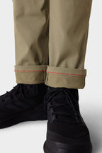 Close-up of a person wearing the 686 Men's Anything Cargo Pant - Slim Fit in light olive, featuring rolled-up cuffs with a thin orange seam, paired with black athletic sneakers—ideal for adventure.