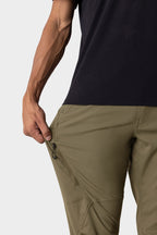 A person in a black shirt and 686 Men's Anything Cargo Pant – Slim Fit in olive green unzips a thigh pocket. Only their torso and arm are visible, emphasizing the utility of these 13-pocket pants for adventure.