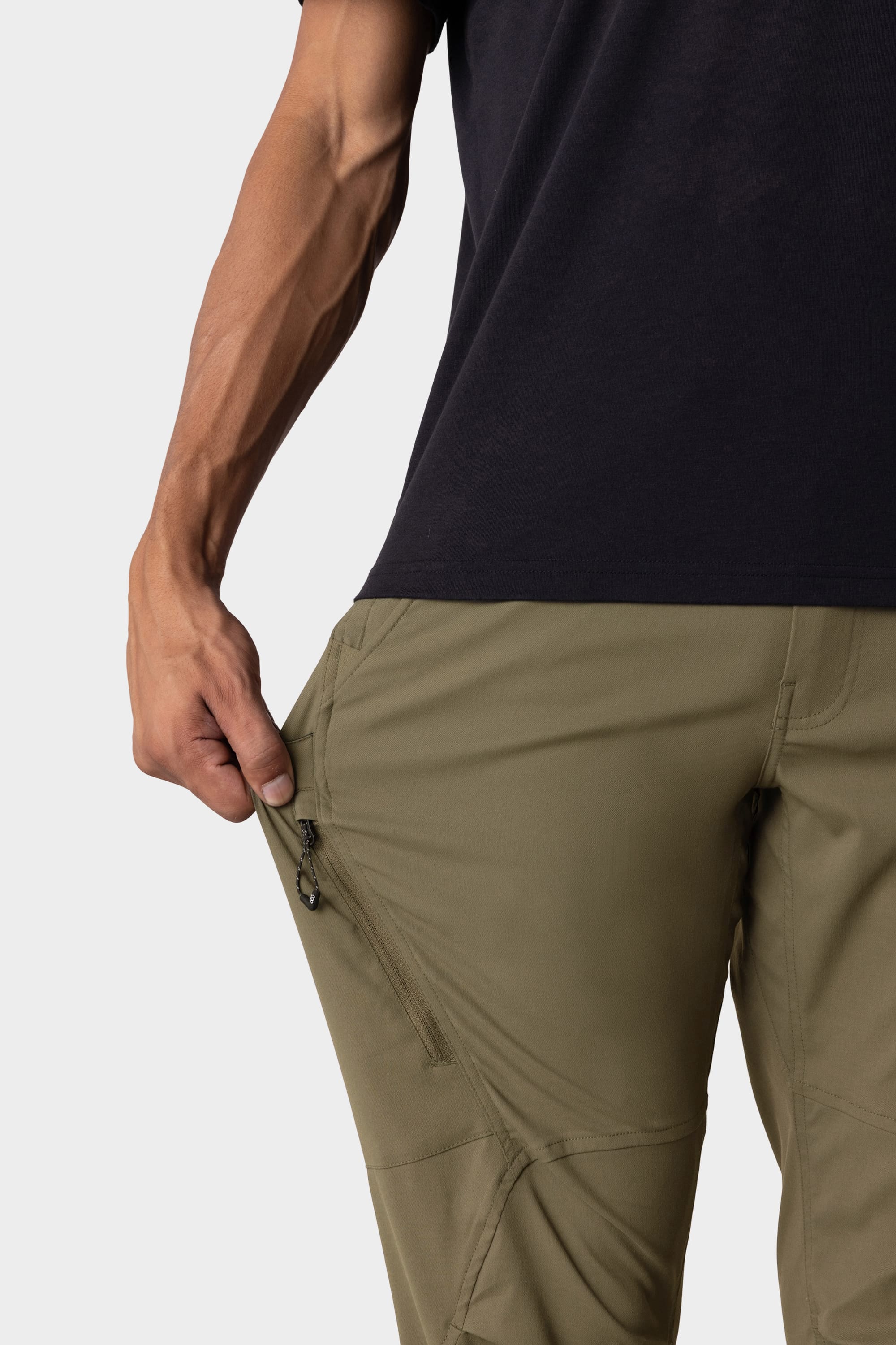 A person in a black shirt and 686 Men's Anything Cargo Pant – Slim Fit in olive green unzips a thigh pocket. Only their torso and arm are visible, emphasizing the utility of these 13-pocket pants for adventure.