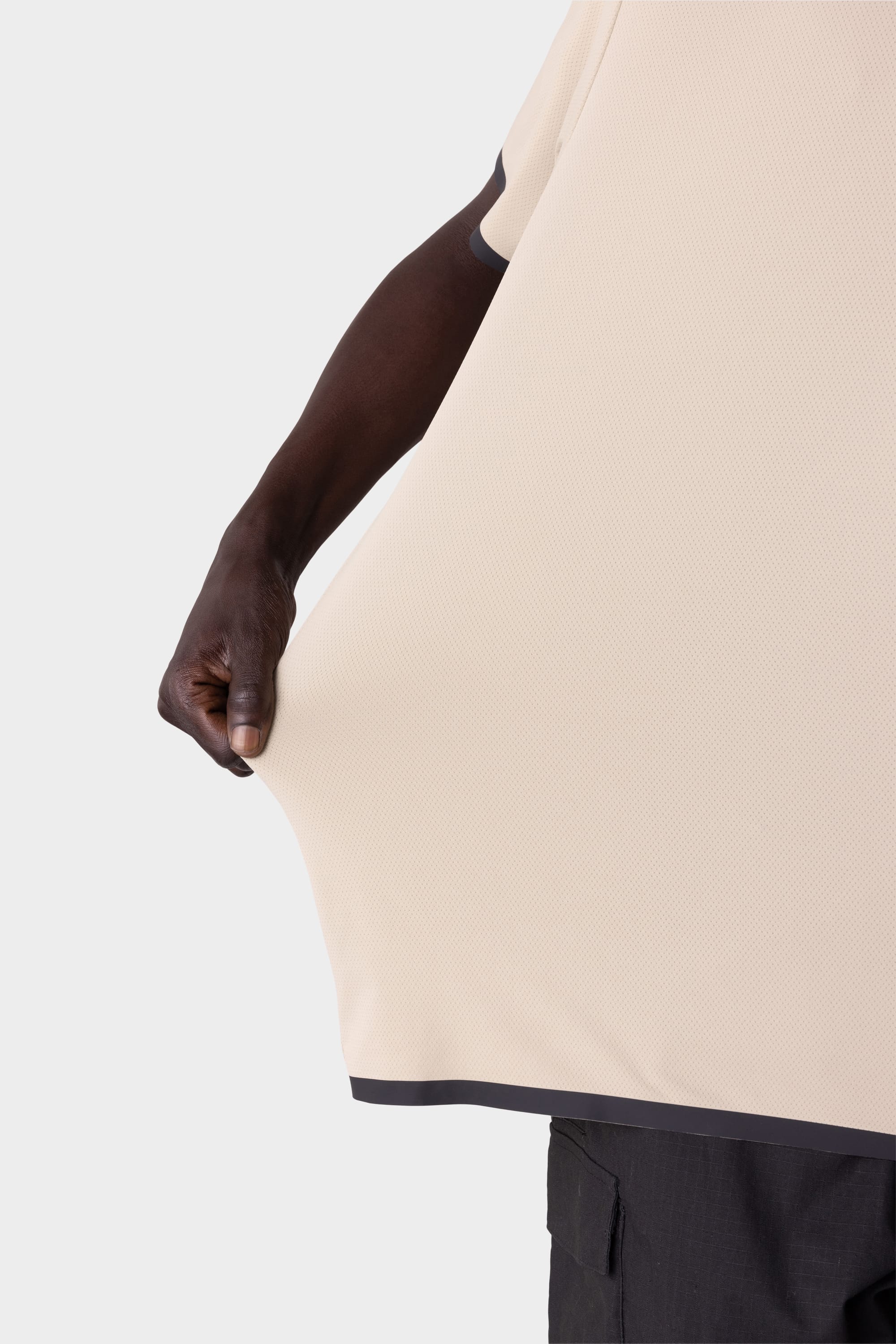 A person demonstrates the stretchiness of the 686 Men's Let's Go Tech Tee by pulling the lightweight fabric outward; only their arm, hand, and part of their body in the dark-trimmed 686 shirt are visible against a plain background.