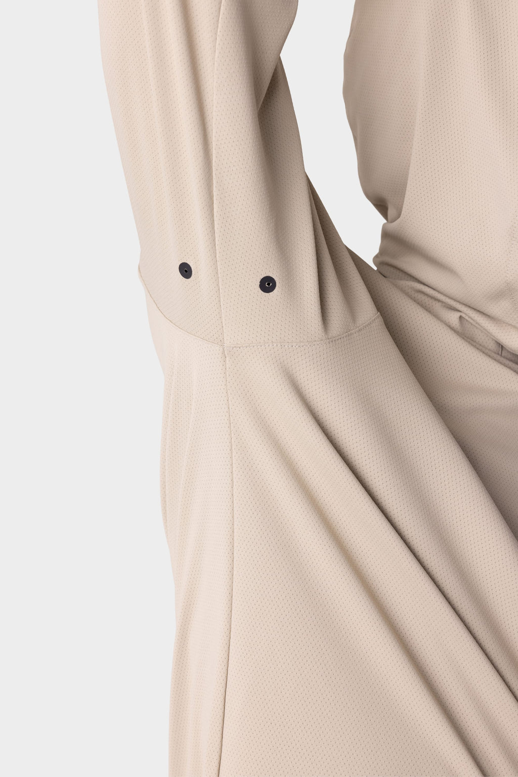 A close-up of the 686 Mens Lets Go Tech Hoody in beige shows its textured, lightweight fabric and a sleeve with two black snap buttons near the cuff, set against a white background.