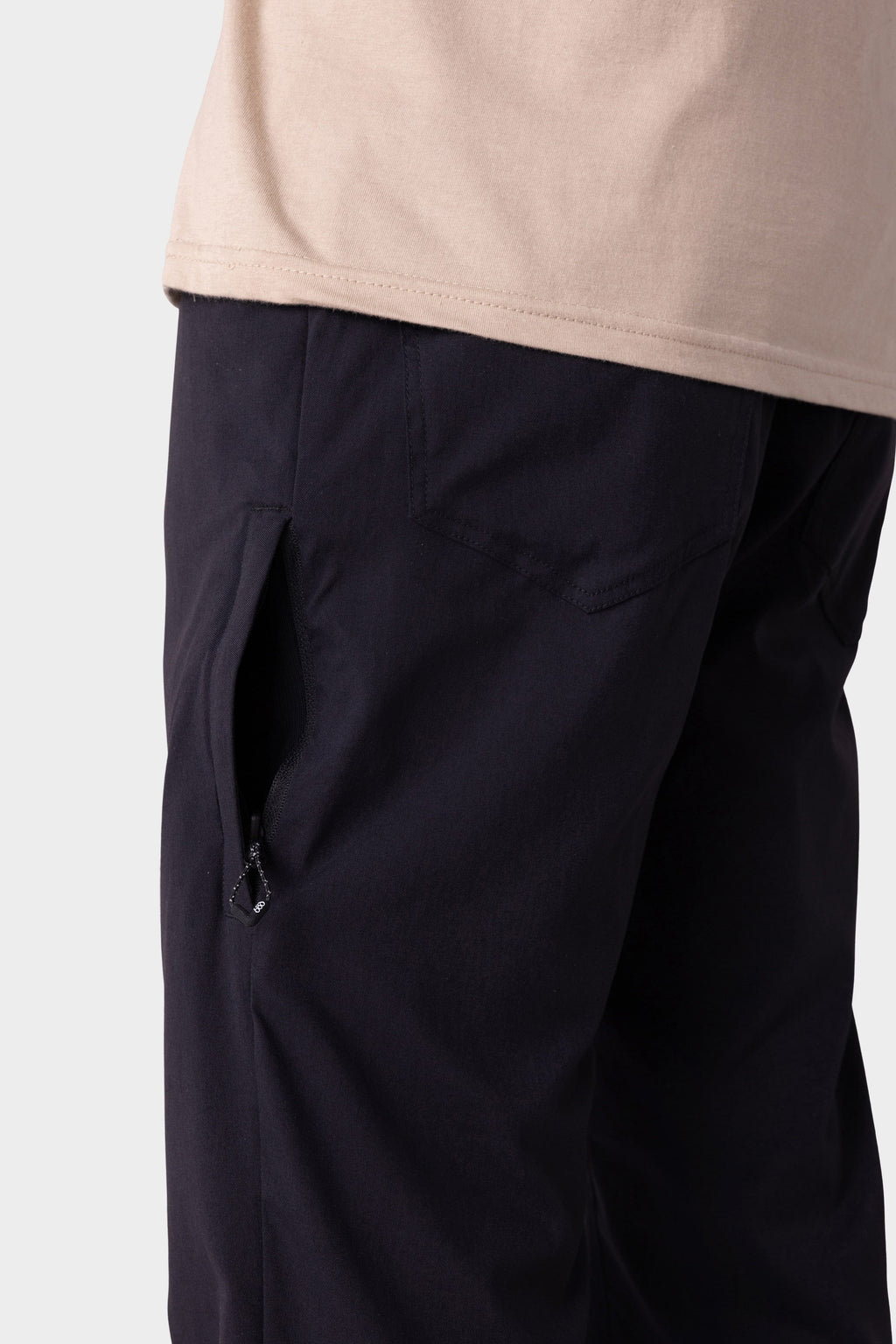 A close-up of a person wearing the 686 Men's Everywhere® Merino-Lined Pant - Relaxed Fit, showcasing a partially unzipped side pocket at the hip and upper leg—ideal for pairing with stylish insulated outerwear against a plain background.