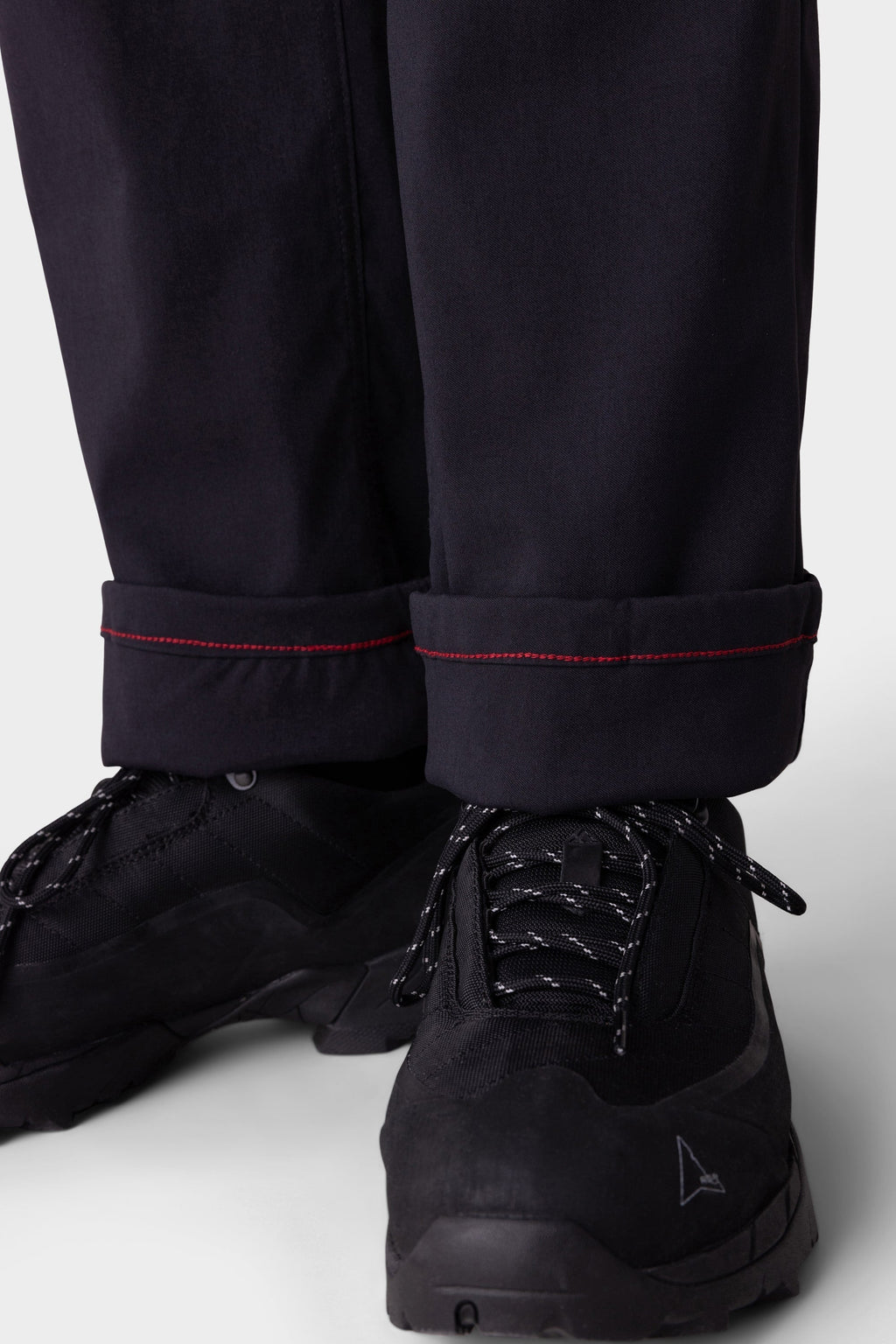 Close-up of a person wearing the 686 Men's Everywhere® Merino-Lined Pant - Relaxed Fit, styled with a warm winter jacket and black athletic shoes. The background is plain and light-colored.