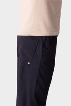A person in 686 Men's Everywhere® Merino-Lined Pant - Relaxed Fit, shown from the waist down and side view, pairs dark pants with a beige t-shirt and insulated outerwear, hand in pocket.