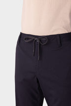A close-up of a person wearing 686 Men's Everywhere® Merino-Lined Pant - Relaxed Fit in dark navy, featuring a drawstring waist and paired with a light beige tucked shirt and insulated outerwear. The focus is on the waistband and upper thigh area.