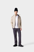 A person stands against a plain background, wearing the 686 Men's Everywhere® Merino-Lined Pant - Relaxed Fit with a white t-shirt, insulated jacket, black shoes, and a black beanie. One hand is in their pocket as they face the camera.