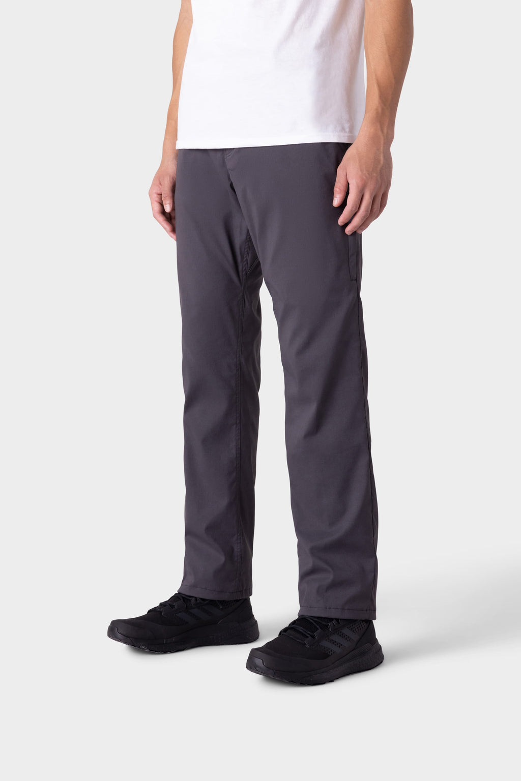 Only the lower half of a person wearing 686 Men's Everywhere® Merino-Lined Pant - Relaxed Fit (dark gray) is visible, paired with black sneakers and standing against a plain light gray background.